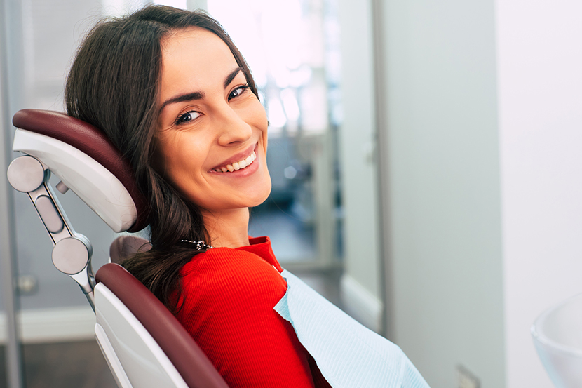 Woman in red shirt smiling in dental chair at modern dentistry office.